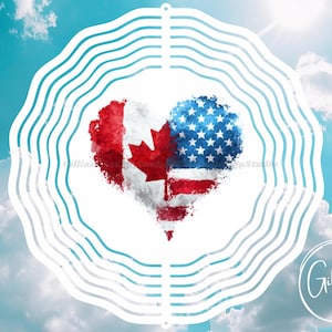 May include: A heart-shaped design featuring the flags of Canada and the United States, set against a blue sky with clouds. The Canadian flag is on the left, and the American flag is on the right. The design is surrounded by a white, wavy border.