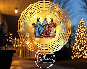 May include: A gold metal wind spinner with three wise men holding gifts. The wise men are depicted in a stained glass style with colorful robes and halos. The wind spinner has a circular shape with multiple layers of metal.