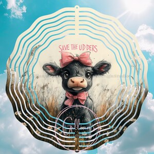 May include: A metal wind spinner with a black and white cow illustration wearing a pink bow. The spinner has a white background with blue and white stripes. The text "SAVE THE UDDERS" is printed on the spinner.