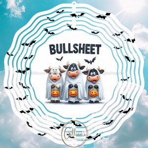 Op de afbeelding: Een Halloween-ontwerp met drie cartoonkoeien verkleed als geesten, elk met een pompoenlantaarn. Het woord "BULLSHEET" staat boven de koeien. Het ontwerp is omlijst door een witte en blauwe cirkelvormige rand met vleermuissilhouetten.
