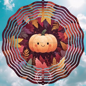 Op de afbeelding: Een grillige windspinner met een herfstthema met een lachende pompoen omringd door kleurrijke herfstbladeren. Het ontwerp is geplaatst tegen een achtergrond van een blauwe lucht met wolken. De tekst "Gillian's Design Studio" staat onderaan.