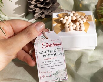 Peut inclure: Une boîte cadeau blanche avec un ruban doré et une étoile en bois. Une étiquette blanche avec du texte rouge indique "I'm dreaming of a Christmas Simmering Potpourri" avec des instructions et une signature "With Love, Hassata B."