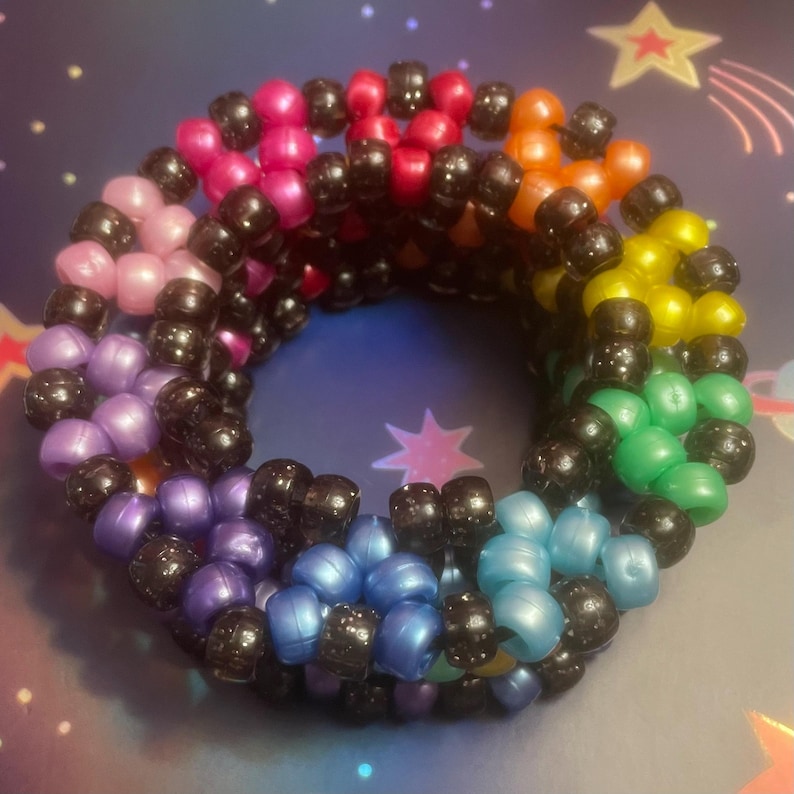 Pode incluir: Uma pulseira de contas coloridas com um design de arco-&iacute;ris. A pulseira apresenta uma variedade de cores, incluindo rosa, vermelho, laranja, amarelo, verde, azul e roxo, separadas por contas pretas. A pulseira &eacute; redonda e parece ser feita &agrave; m&atilde;o.