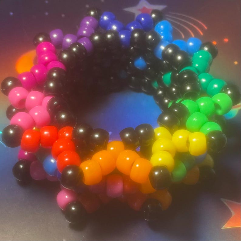 Pode incluir: Uma pulseira colorida de contas com um arco-&iacute;ris de cores, incluindo rosa, vermelho, laranja, amarelo, verde, azul, roxo e preto. A pulseira &eacute; feita de pequenas contas redondas unidas para formar um formato circular.