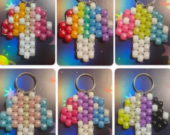 May include: Six colorful beaded keychains in the shape of a mushroom. Each keychain features a different color combination of beads, including pink, blue, yellow, green, purple, and black.