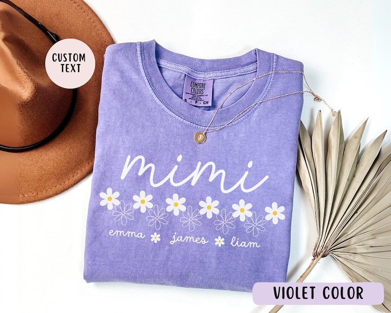 May include: Purple t-shirt with the word "mimi" and a row of white daisies. Below the daisies are the names "emma", "james", and "liam".