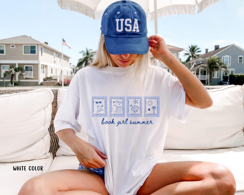 May include: White t-shirt with a blue graphic of four summer-themed images and the text "book girl summer." The shirt is paired with a blue baseball cap with "USA" in white letters.