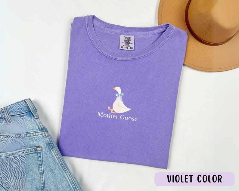 May include: A purple t-shirt featuring a white goose illustration and the text "Mother Goose" printed on the front. The t-shirt is made from a soft, comfortable cotton blend.