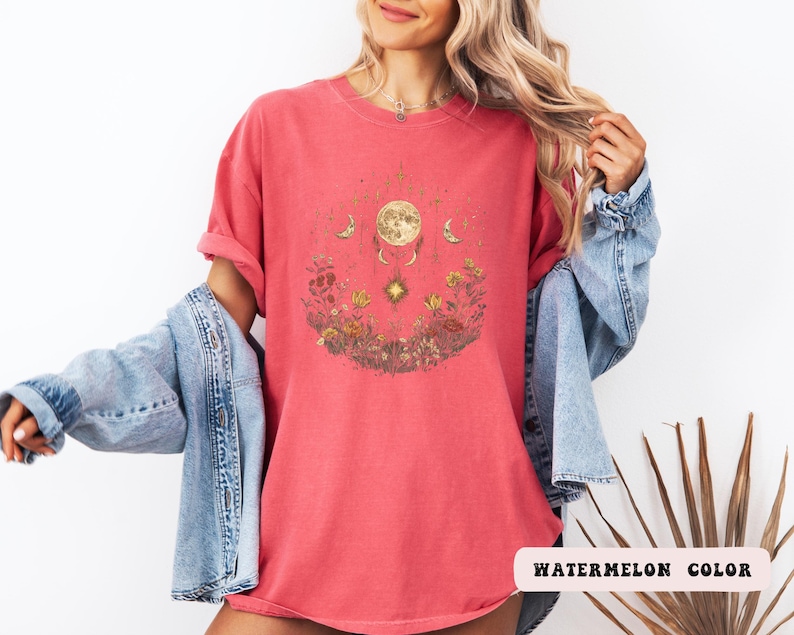 Może przedstawiać: Czerwony T-shirt z grafiką przedstawiającą księżyc, gwiazdy i kwiaty. Tekst "WATERMELON COLOR" jest widoczny w prawym dolnym rogu obrazu.