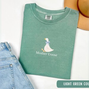 May include: A light green t-shirt with a white goose illustration and the text "Mother Goose" printed on the front.