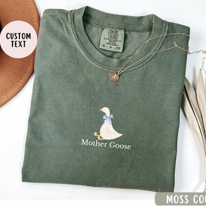 May include: A moss green t-shirt with a white goose illustration and the text "Mother Goose".