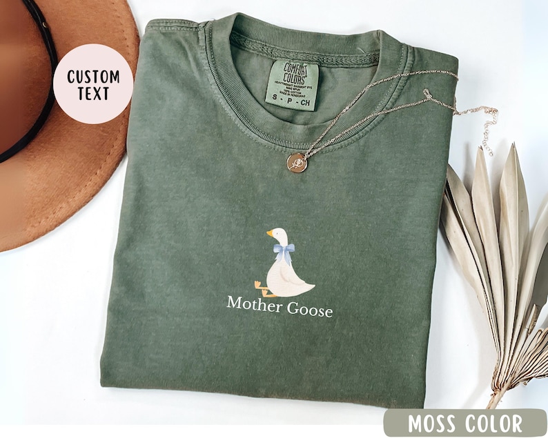 May include: A moss green t-shirt with a white goose illustration and the text "Mother Goose".