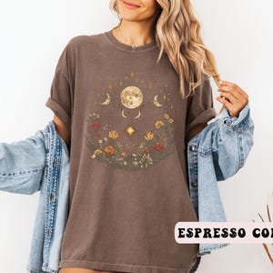 Może przedstawiać: Brązowa koszulka z nadrukiem księżyca, gwiazd i kwiat&oacute;w. W prawym dolnym rogu widoczny jest napis "Espresso Color".