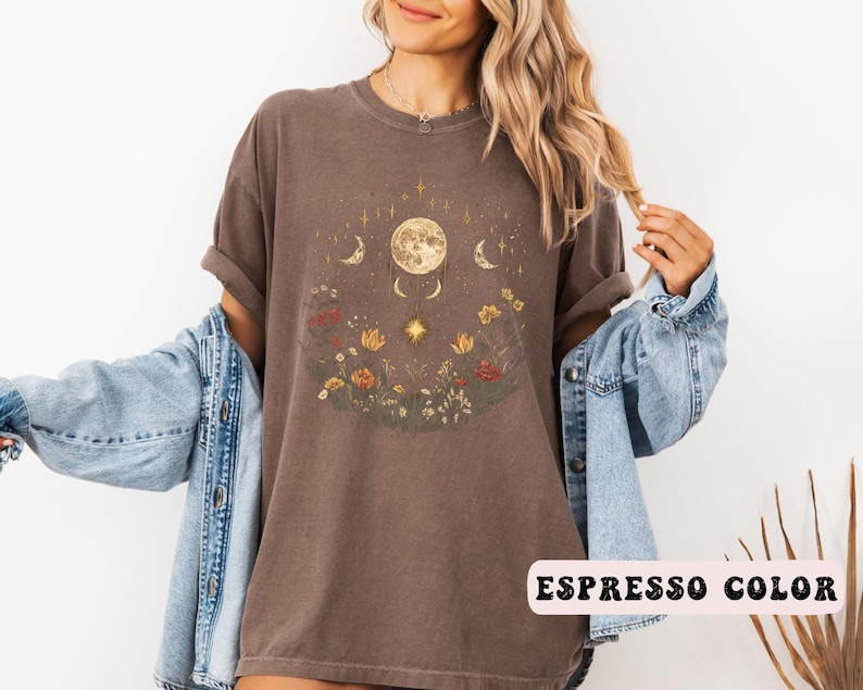 Może przedstawiać: Brązowa koszulka z nadrukiem księżyca, gwiazd i kwiat&oacute;w. W prawym dolnym rogu widoczny jest napis "Espresso Color".