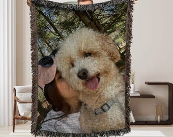 May include: A woven throw blanket with a photo of a person and a dog. The photo shows a person holding a dog in their arms. The dog is a small, white, fluffy dog with its tongue sticking out. The background of the photo is a forest.