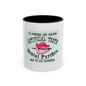 May include: White ceramic mug with a black interior rim. The mug features a vintage advertisement for "Artificial Teeth" with a red denture illustration and text that reads "Dental Purifico."