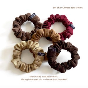May include: Five scrunchies in various shades of brown and tan are displayed on a white surface. Each scrunchie has a tag that reads "chunky ties." The image includes text that says "Set of 2 - Choose Your Colors" and "Shown: All 5 available colors."