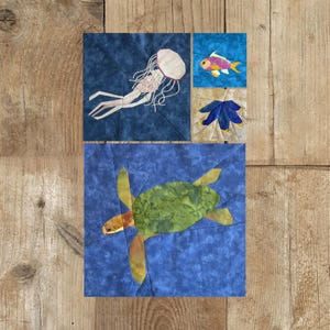 以下が含まれることがあります： 海の生き物をデザインした4つの布の正方形。ピンクの頭と白い触手を持つクラゲ、カラフルな魚、青い花、緑色の甲羅と黄色のひれを持つウミガメが特徴です。