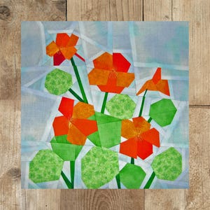 Könnte beinhalten: Ein farbenfroher Patchwork-Quiltblock mit orangefarbenen und roten Blumen und grünen Blättern. Die Blumen bestehen aus Stoffquadraten, die in einem geometrischen Muster zusammengenäht sind.