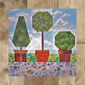 Op de afbeelding: Drie gepotte topiary bomen met verschillende vormen en groen blad. De bomen staan in terracotta potten met bruine, rode en witte patronen. De bomen staan op een achtergrond van grijze stenen.