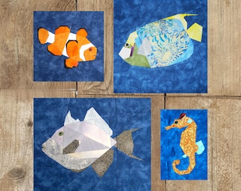May include: Four fabric art squares featuring sea creatures on blue backgrounds. A clownfish with orange and white markings, a fish with blue and yellow patterns, a silver fish, and an orange seahorse with blue accents.