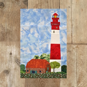 Puede incluir: Un faro rojo y blanco con una ventana amarilla se alza alto contra un cielo azul con nubes blancas. Una pequeña casa de ladrillo rojo con un techo marrón se encuentra frente al faro, rodeada de arbustos verdes y flores.