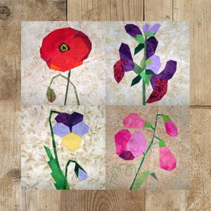 以下が含まれることがあります： 4つの異なる花のデザインが施されたパッチワークキルトブロック。左上のブロックは赤いポピー、右上のブロックは紫色のスイートピー、左下のブロックは紫と黄色のパンジー、右下のブロックはピンクのスイートピーを表しています。