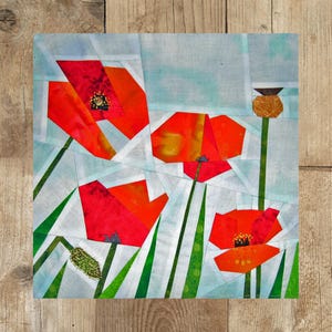 Könnte beinhalten: Ein Patchwork-Deckenbild mit roten Mohnblumen mit grünen Stielen und Blättern auf hellblauem Hintergrund.