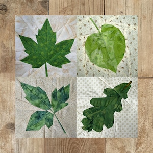 Könnte beinhalten: Ein Patchwork-Quiltblock mit vier verschiedenen grünen Blattdesigns. Die Blätter sind aus Stoff gefertigt und zu einem einzigartigen und schönen Design zusammengenäht.