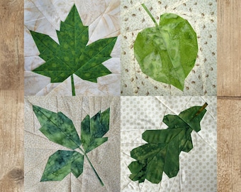 Puede incluir: Un bloque de colcha de retazos con cuatro diseños diferentes de hojas verdes. Las hojas están hechas de tela y están cosidas juntas para crear un diseño único y hermoso.