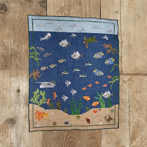 May include: A blue and green quilted wall hanging depicting an underwater scene with various fish, seahorses, and a turtle. The bottom of the scene shows a sandy seabed with starfish, seashells, and an octopus.