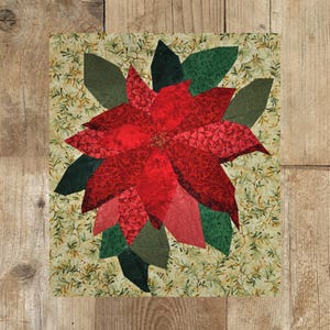 Könnte beinhalten: Eine rote Weihnachtsstern-Blume mit grünen Blättern ist auf einem cremefarbenen Hintergrund mit grünem Blumenmuster appliziert. Der Weihnachtsstern ist aus Stoff gefertigt und hat eine strukturierte Optik.