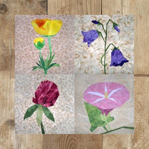 Könnte beinhalten: Ein Patchwork-Quiltblock mit vier verschiedenen Blumendesigns. Der Block oben links zeigt eine gelbe Mohnblume, der Block oben rechts zeigt violette Glockenblumen, der Block unten links zeigt eine rote Blume und der Block unten rechts zeigt eine rosafarbene Morgenröte.