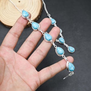 Peut inclure: Un ensemble collier et bracelet en argent orn&eacute; de pierres pr&eacute;cieuses bleues claires en forme de goutte. Les pierres sont serties dans des lunettes en argent et reli&eacute;es par des maillons en argent. Les bijoux sont pr&eacute;sent&eacute;s sur une surface sombre.