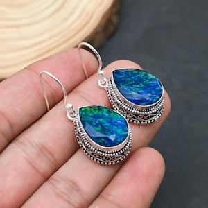 May include: A pair of silver earrings with teardrop-shaped blue and green gemstones. The gemstones are faceted and set in ornate silver bezels. The earrings have a hook closure.