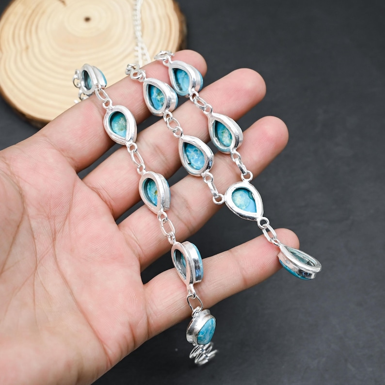 Peut inclure: Un collier en argent orn&eacute; de pierres turquoise en forme de goutte d'eau. Les pierres sont serties dans un cadre argent&eacute; et reli&eacute;es par de petits maillons argent&eacute;s. Le collier est pr&eacute;sent&eacute; sur un fond sombre.