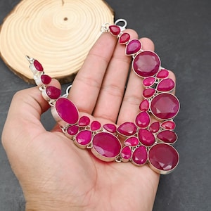 Op de afbeelding: Een opvallende ketting met een verzameling robijn edelstenen in verschillende vormen en maten, gezet in zilver. De ketting toont een reeks dieprode-roze tinten. Het ontwerp is gedurfd en de ketting wordt gepresenteerd tegen een effen achtergrond.