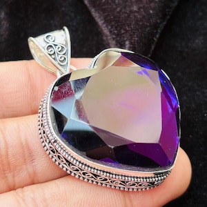 May include: A silver heart-shaped pendant with an intricate filigree design. The pendant features a large, faceted amethyst gemstone in a deep purple hue.