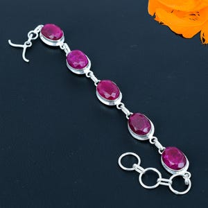 Op de afbeelding: Een zilveren armband met vijf ovale roze edelstenen. De armband heeft een karabijn sluiting en een verstelbare ketting.