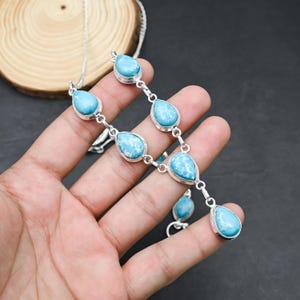 Peut inclure: Un ensemble collier et boucles d'oreilles en argent avec des pierres bleues claires en forme de goutte d'eau et des marbrures blanches. Les pierres sont serties dans des lunettes en argent et reli&eacute;es par des maillons en argent.