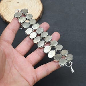 May include: A silver-toned bracelet featuring two parallel rows of oval-shaped, metallic pyrite stones set in polished metal frames. The design includes a secure toggle clasp at one end, showcasing a series of reflective, textured grey-gold stones.