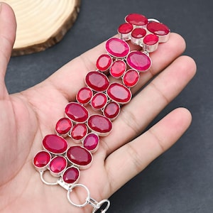 Può includere: Un bracciale in argento con numerose pietre preziose rosse di forma ovale e rotonda. Le pietre sono incastonate in una montatura in argento e disposte in un motivo simmetrico. Il bracciale è mostrato su una mano.