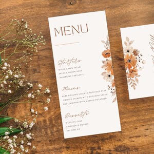May include: A wedding menu card with a floral design in shades of orange and brown. The menu includes starters, mains, and desserts. A matching place card with the name "Mrs. Reacher" is also shown.
