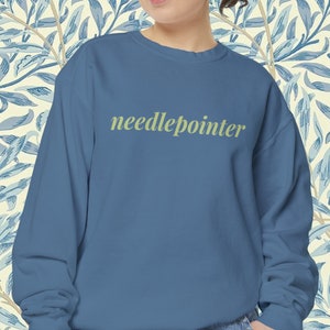 May include: A blue sweatshirt with the text "needlepointer" in a light green color.