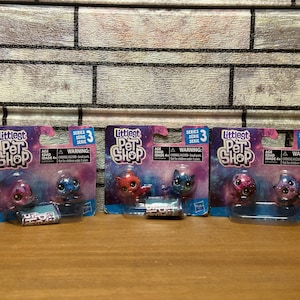 Puede incluir: Tres bolsas ciegas de juguetes Littlest Pet Shop. Cada bolsa presenta un personaje diferente con un tema de galaxia. Los personajes son un gato rosa y azul, un perro azul y morado y un gato rojo y morado. Las bolsas están etiquetadas con el logotipo de Littlest Pet Shop y el número de serie 3.