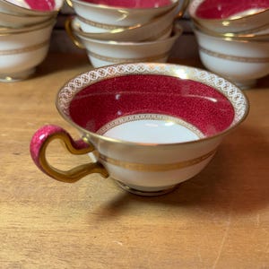 May include: A set of six vintage teacups with a red and white floral pattern and gold trim. The cups are made of fine china and have a delicate design.