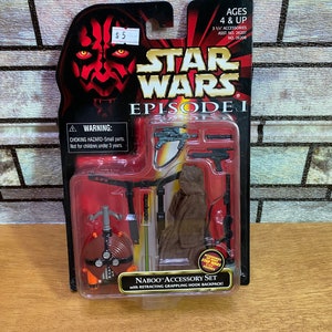 May include: Star Wars Episode I Naboo Accessory Set with a retractable grappling hook backpack. The set includes a brown hooded cloak, a lightsaber, a blaster, and a blaster rifle. The packaging features a red Darth Maul character.