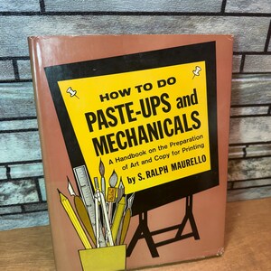 Peut inclure: Un livre vintage intitulé "HOW TO DO PASTE-UPS and MECHANICALS" par S. Ralph Maurello. La couverture présente un design jaune et noir avec des illustrations de fournitures artistiques. Le livre est un manuel pour la préparation de l'art et des copies pour l'impression.