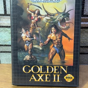 Pode incluir: Um cartucho de jogo Sega Genesis para Golden Axe II. A arte da caixa apresenta um guerreiro, uma guerreira e um dragão.