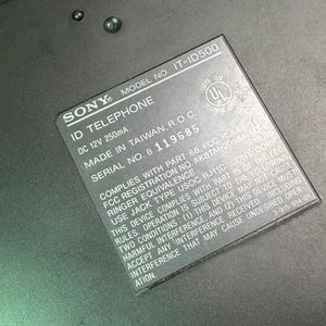 Puede incluir: Primer plano de un tel&eacute;fono ID Sony negro. La etiqueta muestra el n&uacute;mero de modelo IT-ID500, DC 12V 250mA y el n&uacute;mero de serie B 119685. La etiqueta tambi&eacute;n incluye el texto "MADE IN TAIWAN, R.O.C."